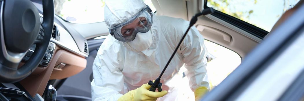 A specialist in a protective suit disinfects the car interior. Antiviral surface treatment. Protective measures during a pandemic