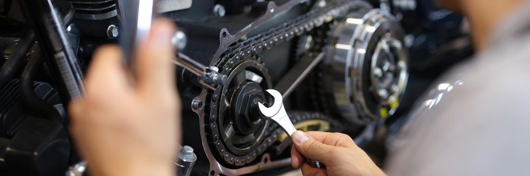 A man spins a detail on a motorcycle with a wrench, close-up. Mechanic works in a garage, maintenance and repair of a motorbike