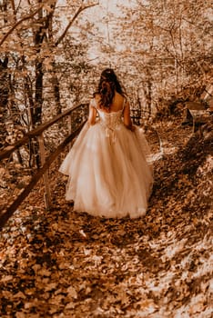 woman bride in white wedding dress with hairstyle makeup and crown on her head walks through autumn forest on fallen orange leaves