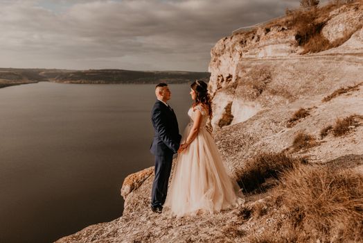 loving couple wedding newlyweds in white dress and suit walk in summer on mountain above river. sunset and sunrise. man and woman on rocks above cliff