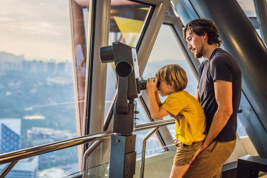 Dad and son are looking at Kuala lumpur cityscape. Us e binoculars. Panoramic view of Kuala Lumpur city skyline evening at sunset viewing skyscrapers building in Malaysia. Traveling with kids concept.