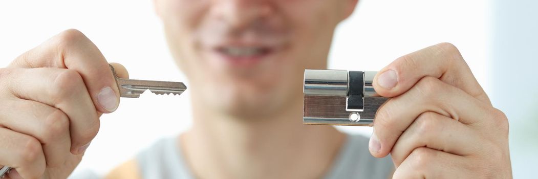 Joyful male locksmith shows a key and a lock, close-up. Apartment castle renovation, protection