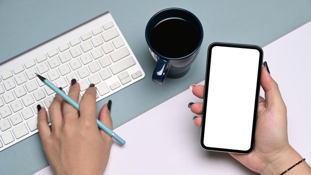 Above view businesswoman holding mobile phone and typing on wireless keyboard.