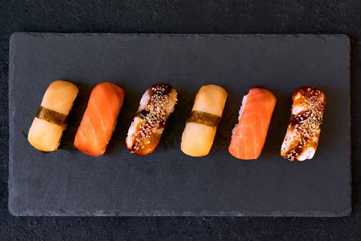 Assorted sushi with salmon, eel and escolar on black stone plate on dark background. Minimal concept. Top view. Flat lay