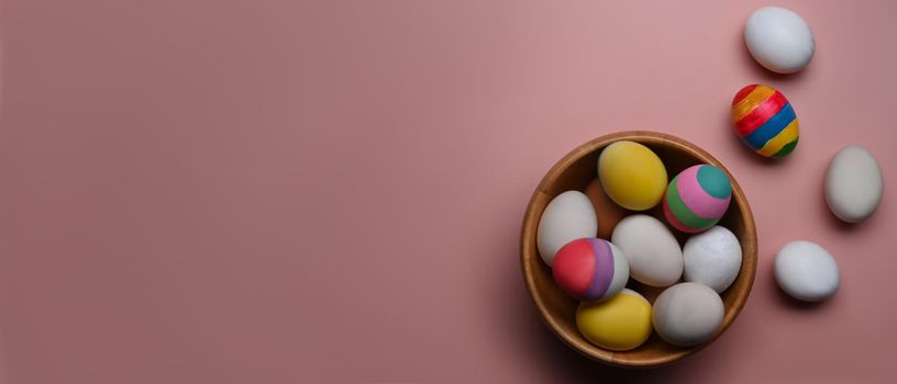 A wooden bowl full of Easter eggs on pink background with copy space for text or design.