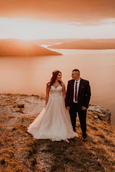 loving couple wedding newlyweds in a white dress and suit walk in the summer on the mountain above the river. sunset and sunrise. man and woman on the rocks above the cliff