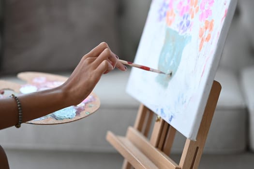 Cropped image of female artist holding palette and painting on canvas.