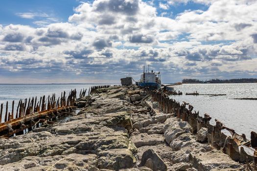 An old abandoned stone pier goes into the sea. An old ship is moored. A sunny day with clouds in Baltiysk, Kaliningrad region, Russia, near the Baltic sea.
