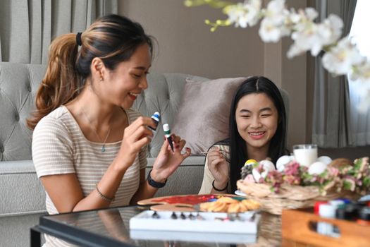 Smiling asian girl and mother painting eggs and preparing for Easter holiday at home together.