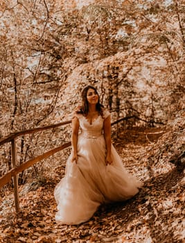 woman bride in white wedding dress with hairstyle makeup and crown on her head walks through autumn forest on fallen orange leaves