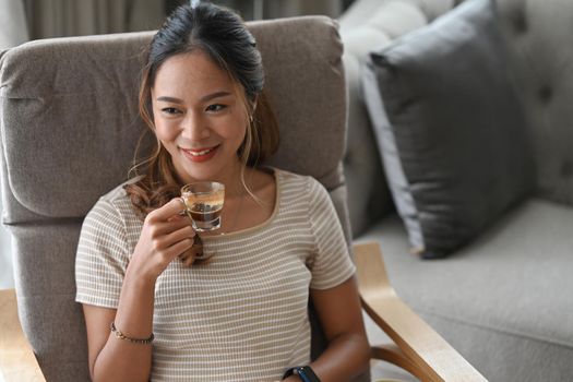 Beautiful young woman relaxing on comfortable armchair at home and drinking coffee.