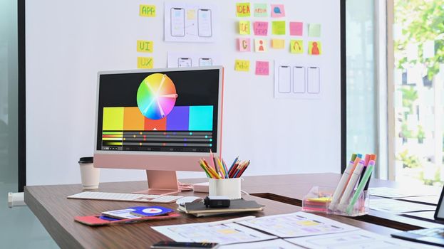 Modern computer with color swatches and wireframe sketches for mobile application on wooden table.