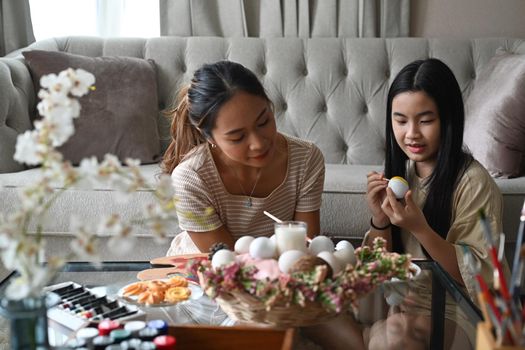 Mom and daughter are spending time together before Easter festival while painting eggs.