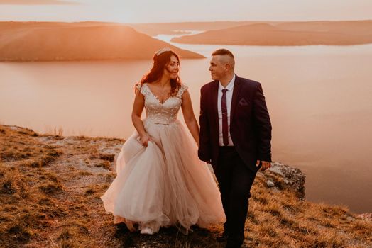 loving couple wedding newlyweds in a white dress and suit walk in the summer on the mountain above the river. sunset and sunrise. man and woman on the rocks above the cliff