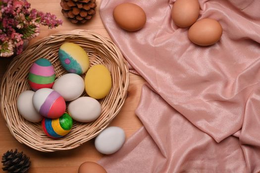 Top view colorful Easter eggs in wicker basket on wooden table. Ester concept.