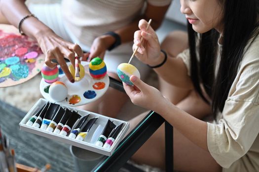 Little girl and mother coloring eggs for Easter festival. Easter, holidays and people concept.