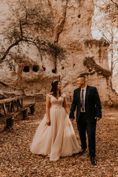 wedding couple in love man and woman walking autumn forest against background of stone rocks. groom suit and bride dress with crown on his head with haircut outdoors. rock monastery bakota