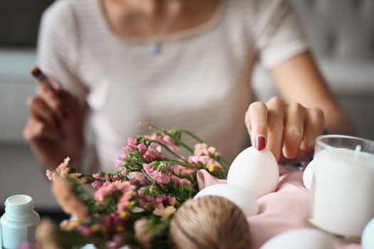 Cropped image of young woman arranging Easter eggs into wicker basket and preparing for Easter celebration.