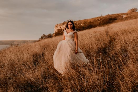 beautiful woman brunette bride in white dress and suit are walking on tall grass in field in summer