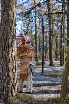 An Indian Native American in a national costume stands in the park among the trees in Svetlogorsk Raushen, Kalinigrad region, Russia, near the Baltic sea. High quality photo.