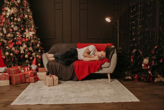 a young man fell asleep on the couch near the christmas tree. decorated house for New Year. Christmas morning. apartment interior. Valentine's Day celebration