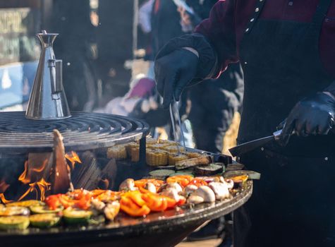 The cook cooks vegetables on the grill on the fire. Fish Festival in Svetlogorsk Raushen, Kalinigrad region, Russia, near the Baltic sea. High quality photo.