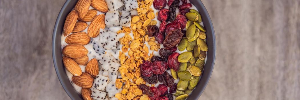 Mango smoothies bowl with almond, dragon fruit, dried cherries, pumpkin seeds and granola on wooden background. BANNER, LONG FORMAT