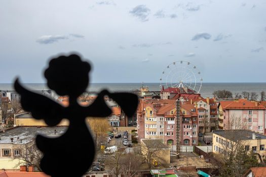 Angel on the background of a panoramic view of the city center, the sea and the Ferris wheel in Zelenogradsk, Kaliningrad region, Russia, near the Baltic sea.