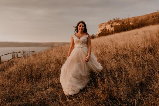 beautiful woman brunette bride in white dress and suit are walking on tall grass in field in summer