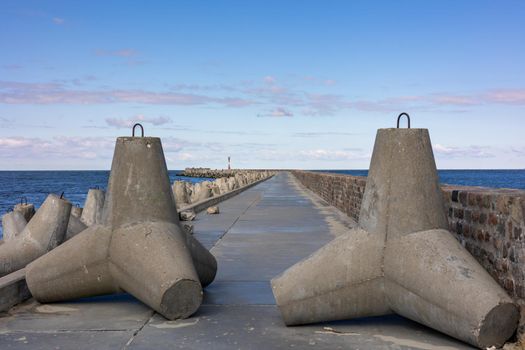 A concrete pier with a brick fence goes into the sea. A clear sunny day and a blue sky with clouds in Baltiysk, Kaliningrad region, Russia, near the Baltic sea.