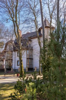 A low beautiful modern house is located behind green fir trees in spring in sunny weather in Svetlogorsk Raushen, Kalinigrad region, Russia, near the Baltic sea. High quality photo.