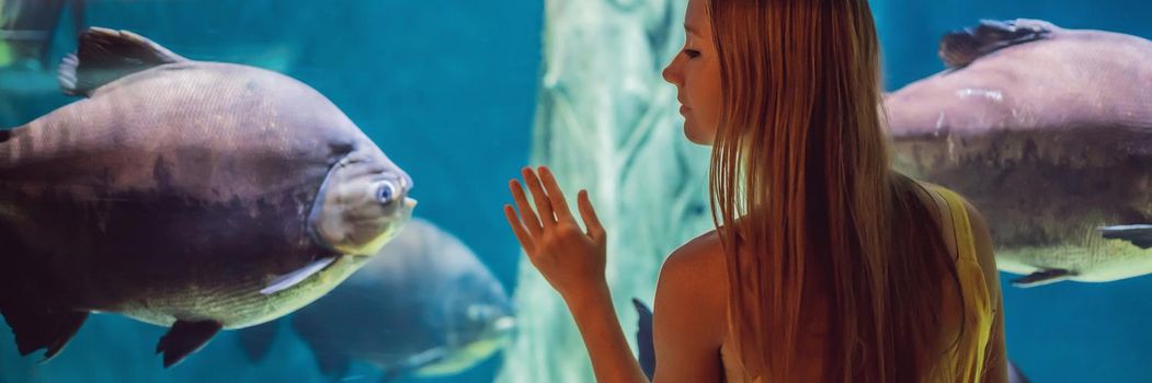 Young woman touches a stingray fish in an oceanarium tunnel. BANNER, LONG FORMAT