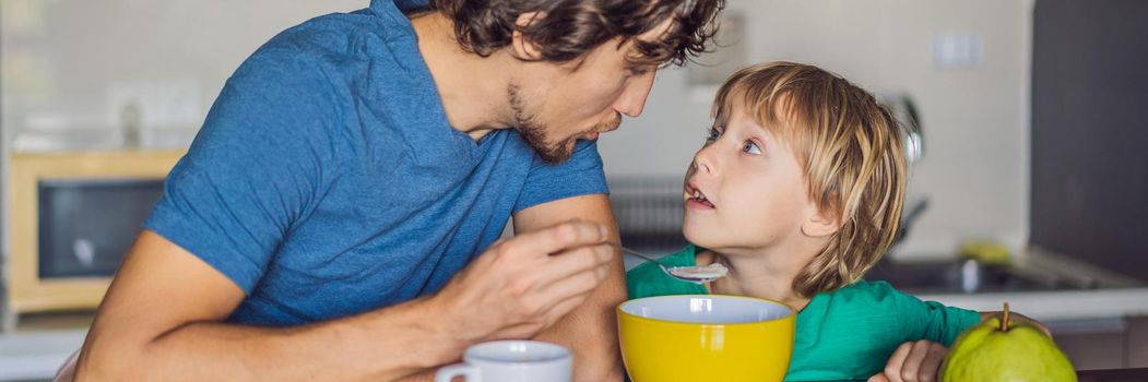 Father and son are talking and smiling while having a breakfast in kitchen. BANNER, LONG FORMAT