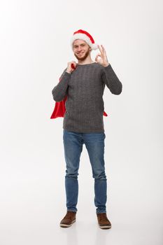 Christmas concept - Young confident smart man holding red big santa bag and giving ok sign.