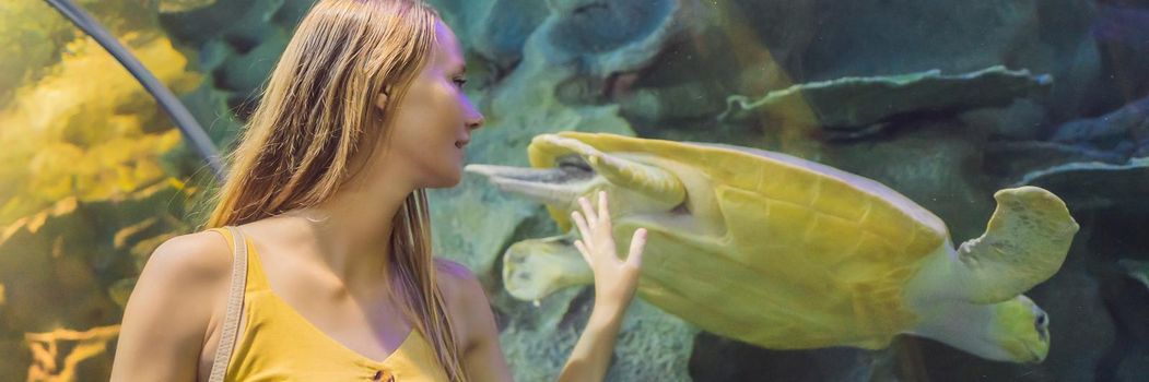 Young woman touches a stingray fish in an oceanarium tunnel. BANNER, LONG FORMAT