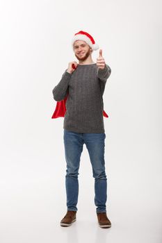 Christmas concept - Young confident smart man holding red big santa bag and giving thumb up.