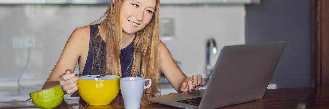 Beautiful woman having coffee and fruits for breakfast and looks into the laptop. BANNER, LONG FORMAT