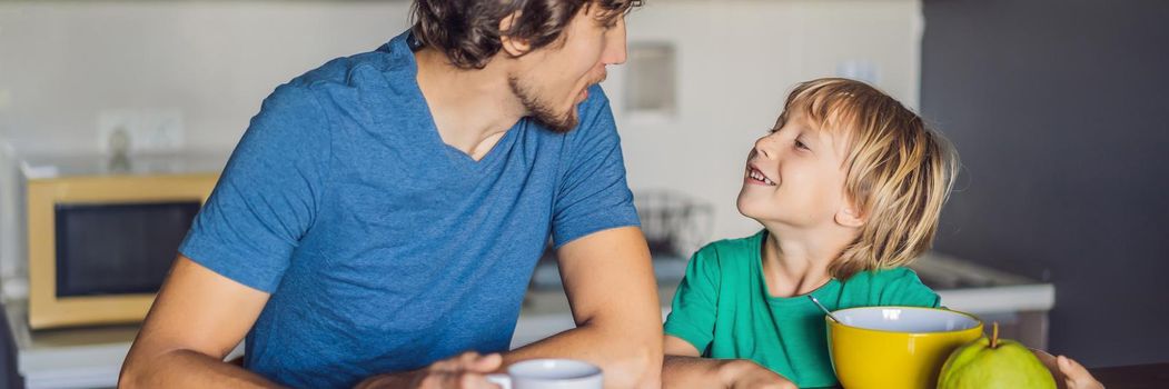 Father and son are talking and smiling while having a breakfast in kitchen. BANNER, LONG FORMAT