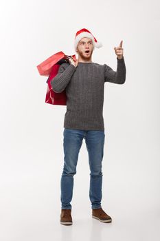 Christmas Concept - attractive young caucasian man surprising shocking holding shopping bag and pointing finger in front.