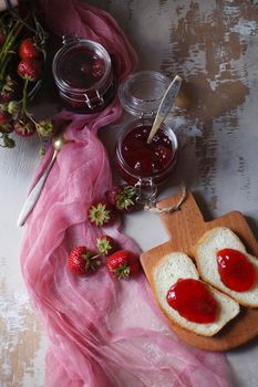 Summer breakfast concept with srawberry jam with bread and fresh harvested berries on wooden rustic table with pink cloth, top view, flat lay, selective focus.