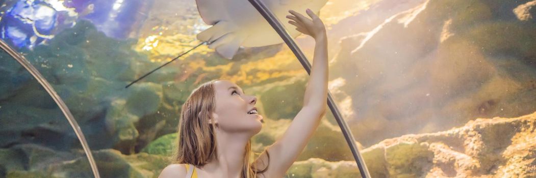 Young woman touches a stingray fish in an oceanarium tunnel. BANNER, LONG FORMAT