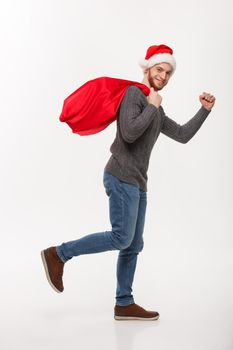 Christmas concept - Young confident beard man running and holding red big santa bag with a lot of present inside.