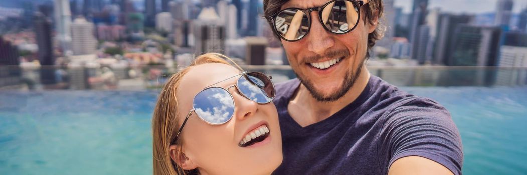 BANNER, LONG FORMAT young happy and attractive playful couple taking selfie picture together at luxury urban hotel infinity pool and panoramic view of the city enjoying holidays honeymoon travel in diversity ethnicity and love.