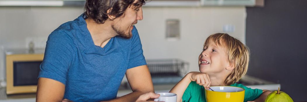 Father and son are talking and smiling while having a breakfast in kitchen. BANNER, LONG FORMAT