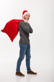 Christmas concept - Young confident smart man holding red big santa bag with a lot of present inside.