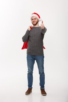 Christmas concept - Young confident smart man holding red big santa bag and giving thumb up.