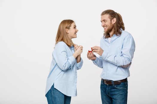 Proposal concept - Portrait of man showing an engagement ring diamond to his beutiful girlfriend over isolated white background .