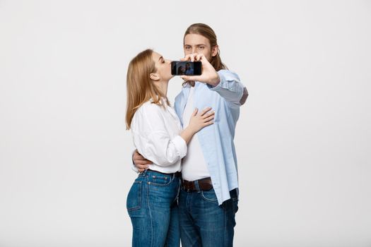 Portrait of a happy couple making selfie photo with smartphone over isolated white studio background