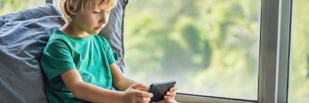 Little blond boy playing games on smartphone. BANNER, LONG FORMAT