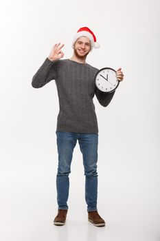 Holiday concept - Young handsome beard man in sweater with white clock giving ok sign.